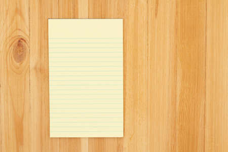 Yellow legal notepad paper with lines on pine wood desk with copy space for your business or writing message or mockupの写真素材
