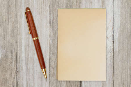 Blank retro old yellowed paper notepad with a pen on weathered woodの写真素材