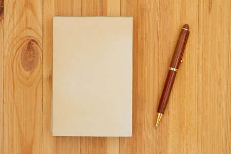 Blank old paper notepad with pen on wood desk with copy space for your messageの写真素材