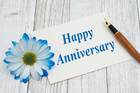 Happy Anniversary message on a white greeting card with a pen with blue daisy on weathered whitewash woodの写真素材