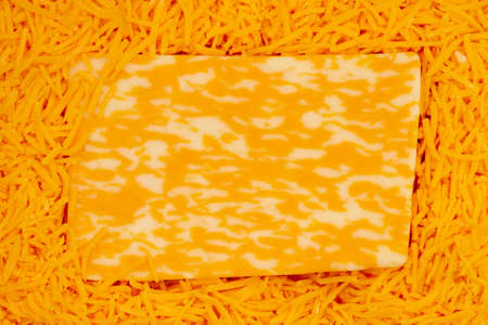 Block of cheese on shredded cheddar cheese background with copy space for your snack message