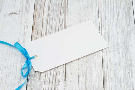 Blank gift tag with a blue ribbon on weathered whitewashed wood desk
