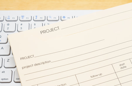 Manila project plan folder with task section on a keyboard on a wood desk