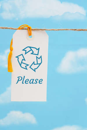 Recycle Please message white gift tag with yellow ribbon over skyの写真素材