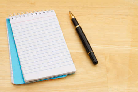 Blank paper notepad with pen on wood desk with copy space for your message
