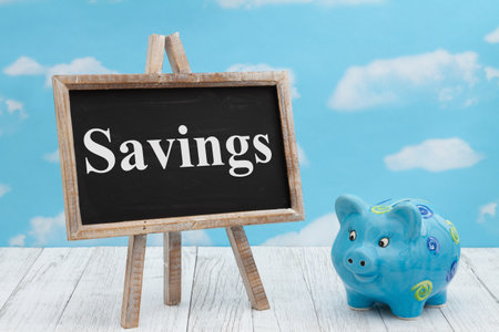 Savings message standing chalkboard with a piggy bank on weathered wood with clear skyの写真素材