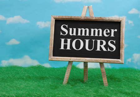 Summer Hours message on standing chalkboard on grass with clear sky