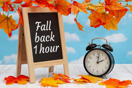 Daylight Saving Time fall back sign with alarm clock and standing blackboard on weathered wood with...