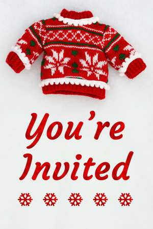 Youâ€™re Invited invitation with red and white Christmas sweater on white plush