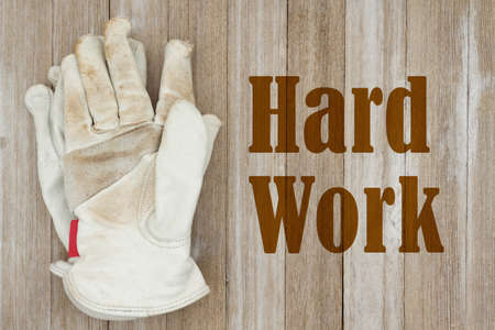 Hard Work message with dirt covered leather work gloves on weathered wood