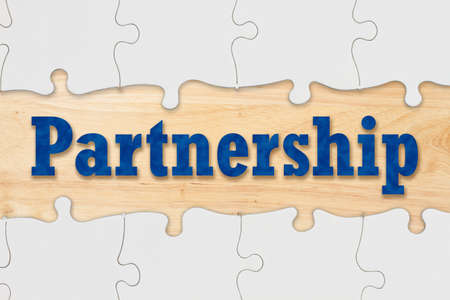 Partnership and teamwork concept coming together with puzzle pieces on a wood deskの写真素材