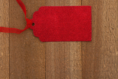 Blank red gift tag on weathered wood with a ribbon for your holiday message