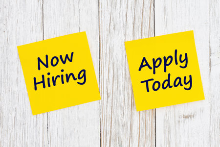 Now Hiring Apply Today message on yellow sticky note on weathered wood for your job noticeの写真素材