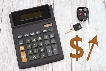The rising costs of cars with dollar sign and arrow with a black calculator with car keys on wood deskの写真素材