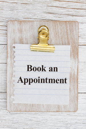 Book an appointment on a weathered wood clipboard with torn paper on weathered wood deskの写真素材