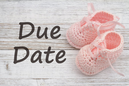 Due date message with pink baby booties on weathered wood