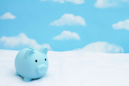 Blue piggy bank on snow with sky with clouds for winter savings with plenty of copy spaceの写真素材