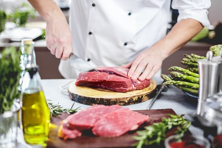 Chef in restaurant kitchen cooking,he is cutting meatの写真素材