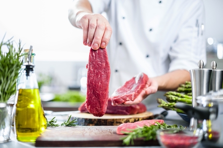 Chef in restaurant kitchen cooking,he is cutting meatの写真素材