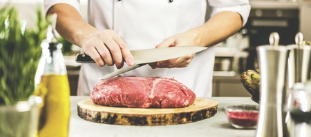 Chef in restaurant kitchen cooking,he is cutting meatの写真素材