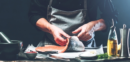 The big salmon is in the hands of the chef cook He is using a knife to slice salmon filletの写真素材