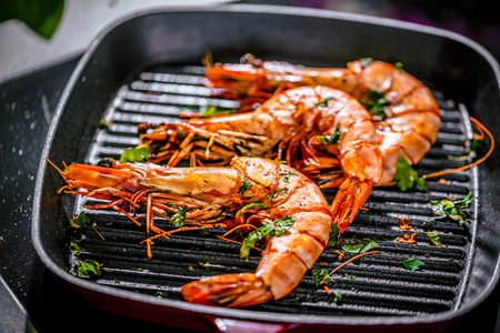 Roasted tiger prawns in iron grilling pan with  lemon, black background, top viewの写真素材