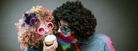 Portrait of party Men and woman in wig and glasses eating Carneval donutの写真素材