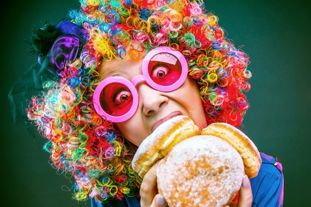 Portrait of beautiful party woman in wig and glasses eating Carneval Donutの写真素材