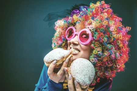 Portrait of beautiful party woman in wig and glasses eating Carneval Donutの写真素材