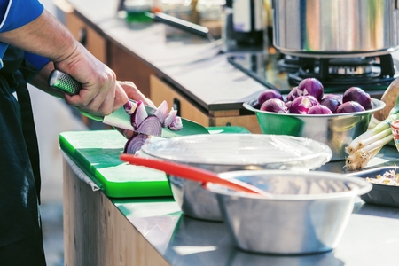 Close up of unrecognizable cook cutting onions and other vegetables with chef knife while workingの写真素材