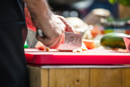 Close up of unrecognizable cook cutting onions and other vegetables with chef knife while working