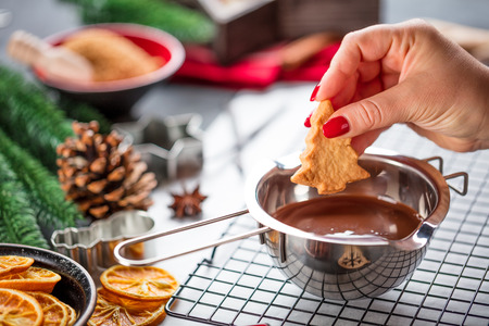 Woman is glazing christmas biscuits with liquid chocolate on a kitchen tableの写真素材