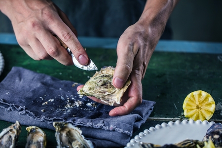 Hands of the cook opening an oyster on wooden Table
