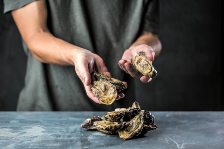 Fresh raw oysters in man hands on dark bakground