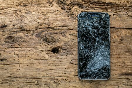 mobile phone with broken touchscreen on wooden background.の写真素材
