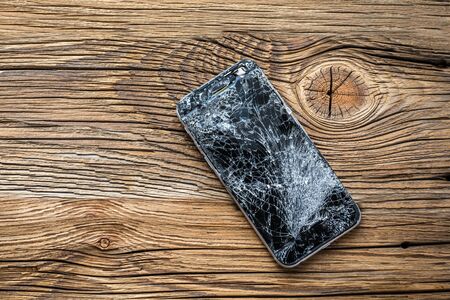 mobile phone with broken touchscreen on wooden background.の写真素材