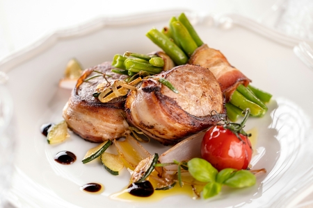 Juicy pork medallions wrapped in bacon, serve on the iron pan on the dark wooden dackground. Close upの写真素材