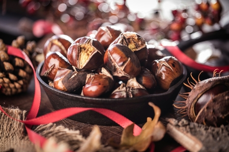 Roasted chestnuts served in a special perforated chestnut pan on an old wooden tableの写真素材