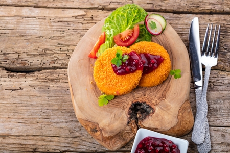 Breaded and baked camembert with cranberry sauce on wooden tabel