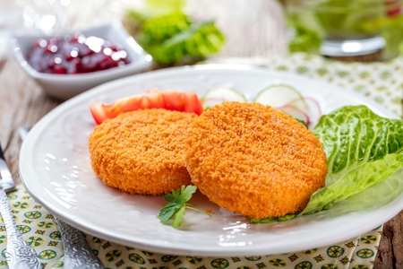 Breaded and baked camembert with cranberry sauce on wooden tabel