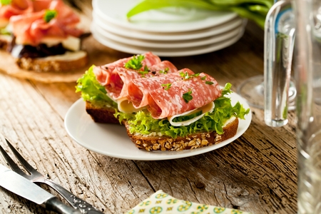 Wholegrain bread with seeds topped with spicy Italian salami sausage and salad on an old grunge rustic wooden boardの写真素材