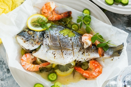 delicious roasted dorado or sea bream fish with lemon and fresh Prawns , fresh parsley and spinach on white platterの写真素材