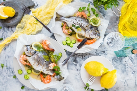 delicious roasted dorado or sea bream fish with lemon and fresh Prawns , fresh parsley and spinach on white platterの写真素材