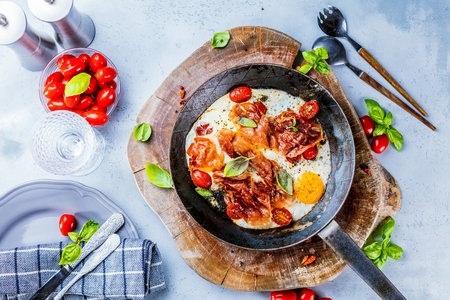 Iron pans and bacon eggs on dark wooden cuting boardの写真素材