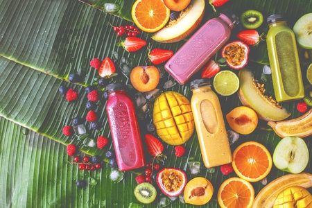 Flat-lay of colorful smoothies in bottles with fresh tropical fruit and superfoods on concrete background.の写真素材