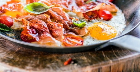 Iron pans and bacon eggs on dark wooden cuting boardの写真素材