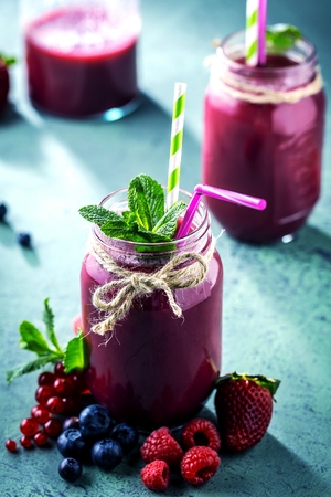 Flat-lay of colorful smoothies in bottles with fresh tropical fruit and superfoods on concrete background.の写真素材