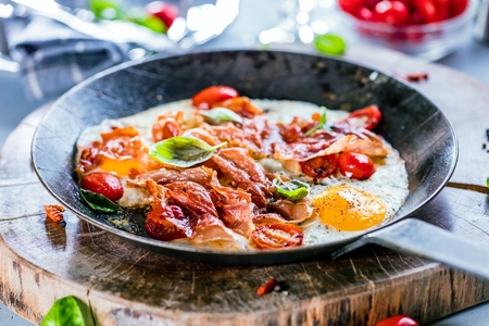 Iron pans and bacon eggs on dark wooden cuting boardの写真素材