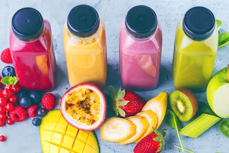 Flat-lay of colorful smoothies in bottles with fresh tropical fruit and superfoods on concrete background.の写真素材