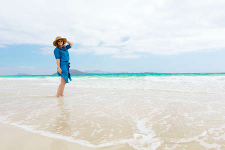 Happy traveler woman in blue dress enjoys her tropical beach vacationの写真素材